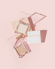 Two powder makeup highlighters on pink background with packaging