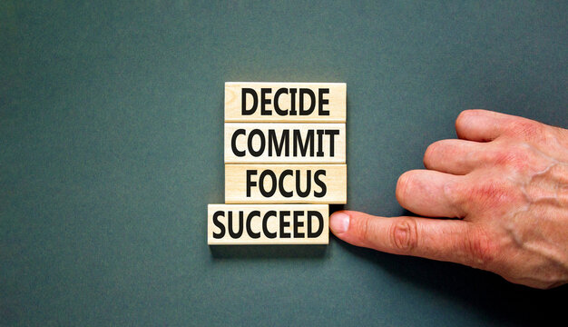 Decide commit focus succeed symbol. Concept word Decide Commit Focus Succeed on wooden block. Beautiful grey background. Businessman hand. Business decide commit focus succeed concept. Copy space.