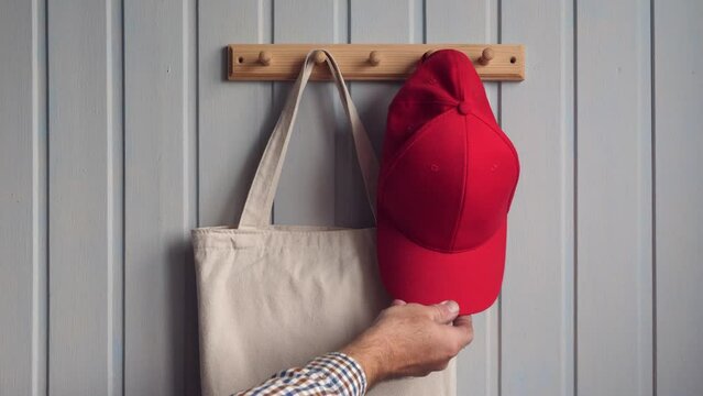 a man hangs a white cloth bag and a red baseball cap on a wooden hanger.