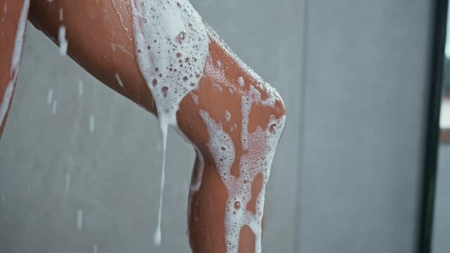 close up woman washing legs holding pink wisp of bast foam pouring in shower cabin wellness and morning routine slow motion