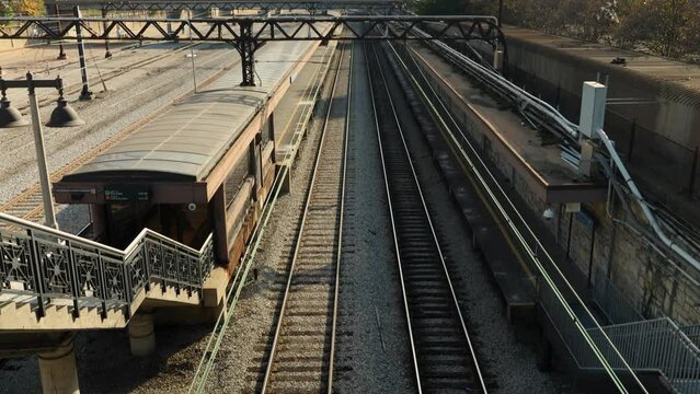 tilt footage of a train station with long railroad tracks on the ground, autumn colored trees, skyscrapers and office buildings in the city skyline at Grant Park in Chicago Illinois USA