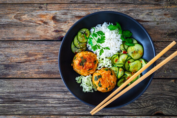 Meatballs served with white rice and marinated sliced cucumber on wooden background
