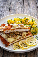 Crispy breaded seared chicken cutlet with fried white mushrooms, cheese and boiled potatoes on wooden table
