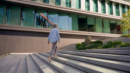 Back view businesswoman middle-aged lady manager CEO entrepreneur leader professional lawyer unrecognizable woman walking outdoors to office building city business center walk up stairs climbing steps