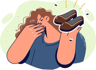 Woman holds smelly shoes and covers nose, disgusted by smell caused by sweating or skin fungus