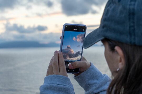 Beautiful view of a woman taking a picture of the sky at the beach with her cell phone