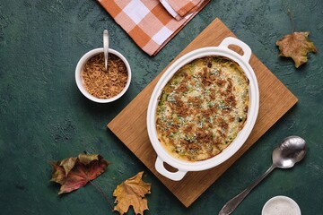 Green bean casserole with creamy sauce topped with crispy fried onions in a white ceramic dish on a green concrete background. Traditional Thanksgiving Dishes. American cuisine.