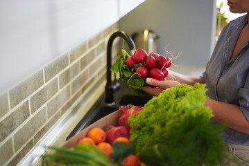 Close-up woman holding radish, standing by kitchen counter with a cardboard box full of delivered fruits and vegetables
