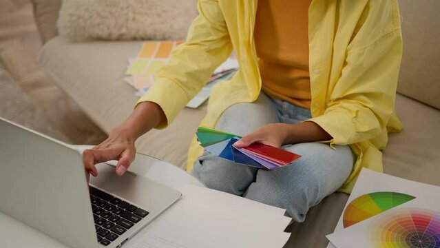 Unrecognizable woman businesswoman graphic designer architect hold multicolored palette catalog samples of rainbow colors wall paint choose color new interior design house renovation working on laptop