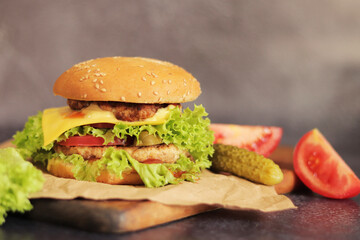Double cheeseburger and vegetables on a gray background. Juicy tasty burger close-up on a wooden cutting board, side view. Fast food