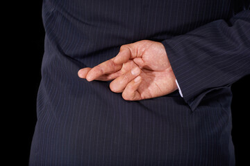 Fototapeta premium Closeup, business and man with fingers crossed, fraud and lawyer with oath, corrupt and dishonesty. Person, corporate professional or model in a suit, hand gesture or liar on a dark studio background