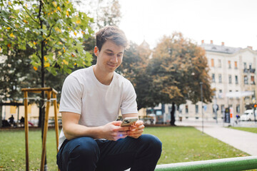 Obraz premium Young adult student using smart phone in park while going to school campus. Connected with friends everywhere, checking online bank, posting stories.