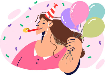 Woman in birthday cap holds balloons and stands among falling confetti during anniversary party