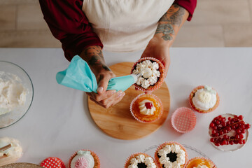 Top view of unrecognizable female confectioner decorating cakes while standing near the table - obrazy, fototapety, plakaty