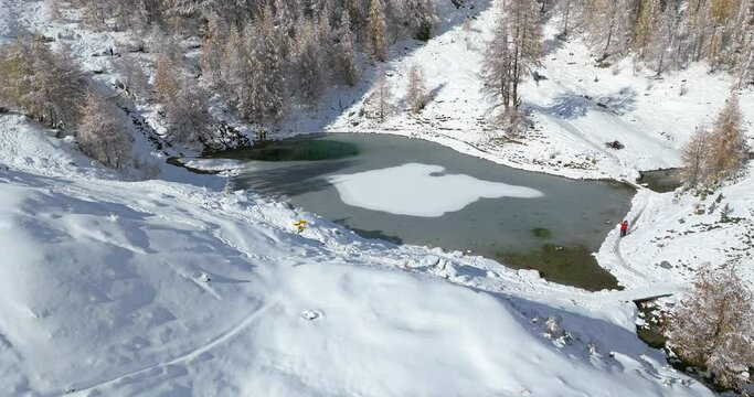 Lac Bleu Arolla lake frost in autumn colors in winter time snow covered Swiss mountains in Switzerland orange colors daylight flowing stream river aerial by drone