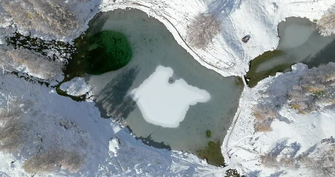 Lac Bleu Arolla lake frost in autumn colors in winter time snow covered Swiss mountains in Switzerland orange colors daylight flowing stream river aerial by drone