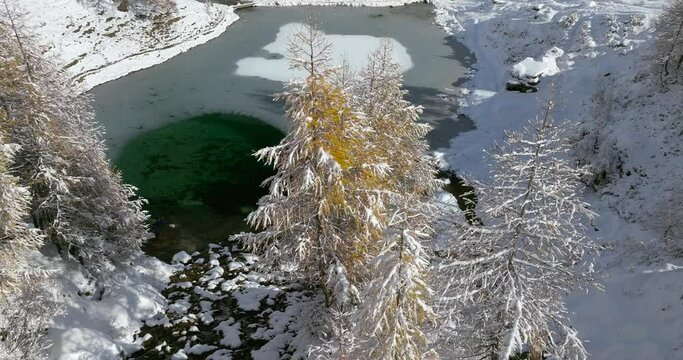 Lac Bleu Arolla lake frost in autumn colors in winter time snow covered Swiss mountains in Switzerland orange colors daylight flowing stream river aerial by drone