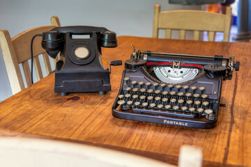 old black typewriter on a vintage wooden table at home , aged rotary crank telephone in the...