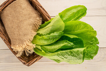 Fresh green salad leaves with white ceramic plate on wooden table, macro, top view.