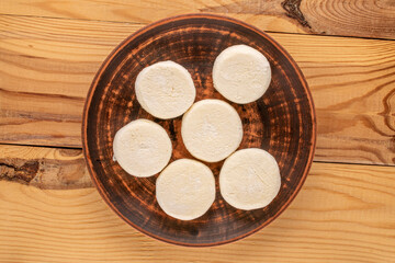 Several frozen semi-finished cheesecakes on a clay plate on a wooden table, macro, top view.
