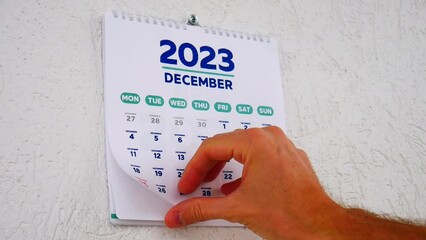 Close-up of a male hand flipping through the December page of 2023 wall calendar followed by the title page of a new 2024 calendar