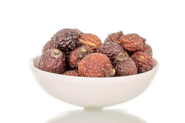 Several dry rosehip berries in a white ceramic saucer, macro, isolated on white background.
