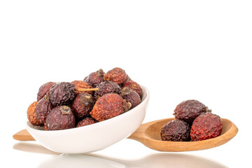 A few dry rosehip berries in a white ceramic saucer with a wooden spoon, macro, isolated on a white background.