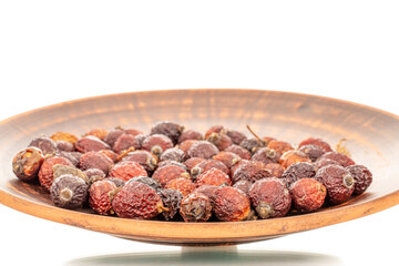 Several dry rosehip berries with clay plate, macro, isolated on white background.