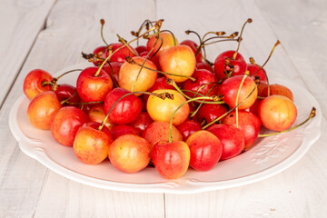 Organic ripe cherry berries with white ceramic plate on wooden table.