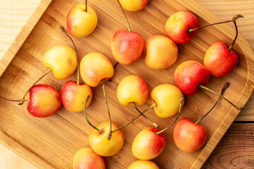 Several cherry berries with bamboo plate on wooden table, macro, top view.