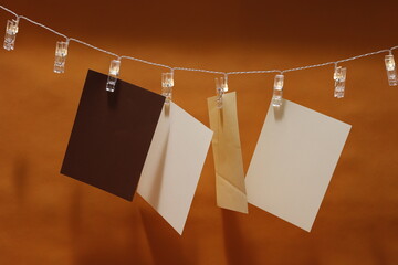 Kartki papierowe zawieszone na łańcuchu świetlnym z klamrami na pomarańczowym tle - obrazy, fototapety, plakaty