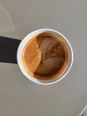 Top view of white paper disposable fresh americano cup on a table on the street under the sun ray.
