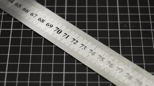 A metal ruler flies into the frame to the mark of 80 centimeters against the background of the grid on the cutting mat.