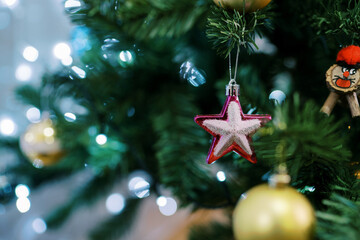 Pink star hangs on a green branch of a Christmas tree among balls and garlands