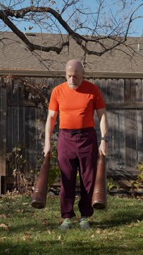 senior, athletic man is exercising with heavy wooden Persian meels in a backyard