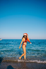 Backside view of bikini woman in Santa hat waving hand standing in the sea