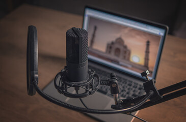 Home studio for podcasts. Large black Microphone on stand, notebook and notebooks on desk. Close-up