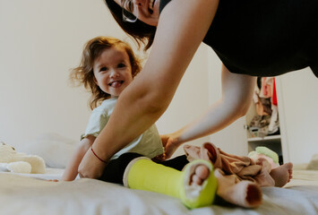 Mom changes clothes for a baby girl with a cast on her leg.