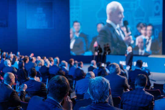 Businessmen Listening To Director Giving Presentation On Projection Screen At Export Forum