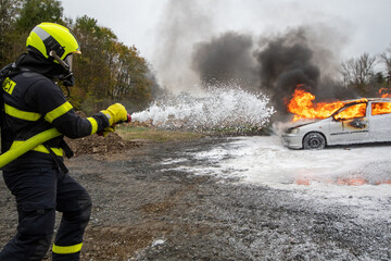 Firefighter uses foam to extinguish a burning vehicle that is engulfed in flames