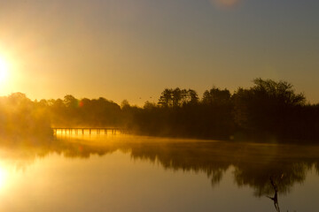 Fototapeta na wymiar Bridge over steaming lake and the sun coming up