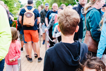 A boy, with his back turned, waits in line for an attraction on his vacation.