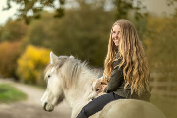 Horse and dog concept: A young female equestrian and her dog on her icelandic horse in front of a...