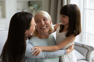Grown daughter and cute little granddaughter hugging smiling mature woman, congratulating with...