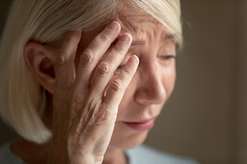 Fototapeta premium Close up unhappy mature woman crying, thinking about problems, frustrated older female suffering from strong headache or migraine, touching forehead, feeling unwell, dementia or mental disorder
