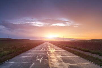 Beautiful shot of a road between green fields under a cloudy sky during a sunset