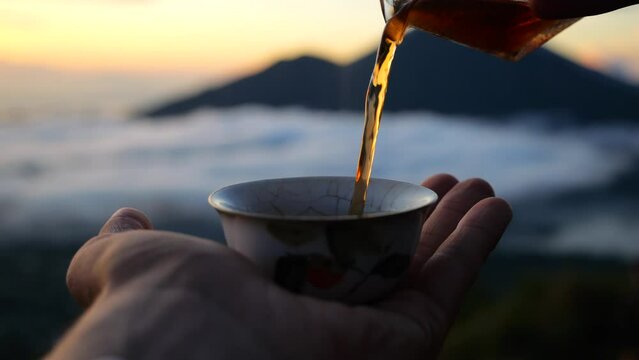 Close-up of hot tea being poured into a tiny porcelain cup in mountains above clouds. Cinematic video unique experience of tea ceremony in mountains. Ideal for those who love tea drinking in mountains