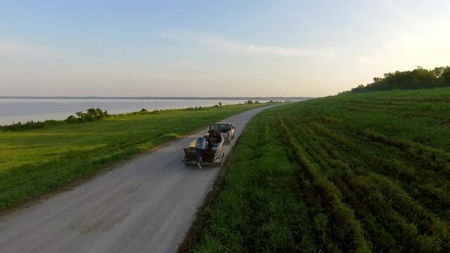 Aerial: Drone Forward Shot Of Pickup Truck Towing Boat On Road In Meadow By Tranquil River Against Sky - Bayou, Louisiana