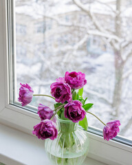 bouquet of dark red lilac tulips in glass vase on windowsill overlooking snowy street. flower bouquet in vase on table. Gift interior decoration. florist, decorator. Flower shop.