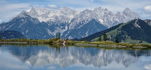 Scenic panoramic shot of a lake reflecting the surrounding plants and mountains in the background